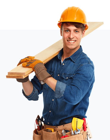 A member of the construction team, wearing a hard hat, gloves, and a tool belt filled with various tools, confidently holds a wooden plank over his shoulder.