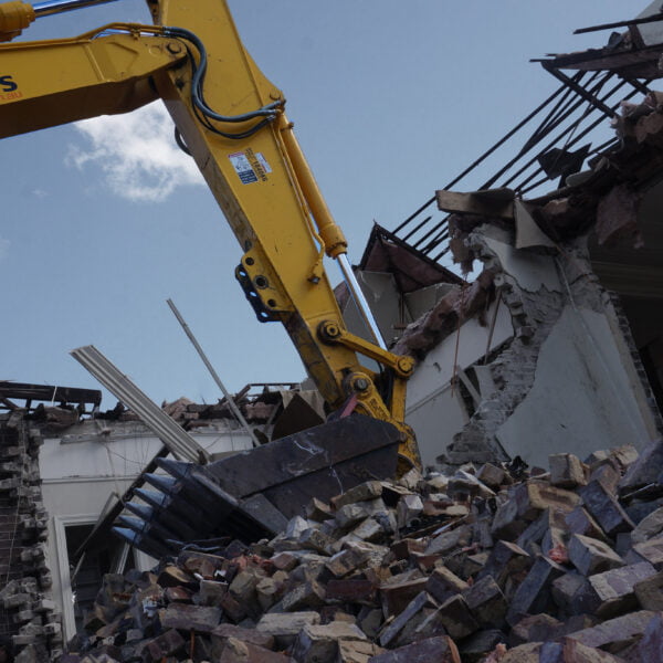 Eastwood, NSW 2122 16 A yellow excavator is engaged in a home demolition, tearing down a brick building with rubble and debris scattered in the foreground. Partly intact sections of the structure remain visible as they are being dismantled.