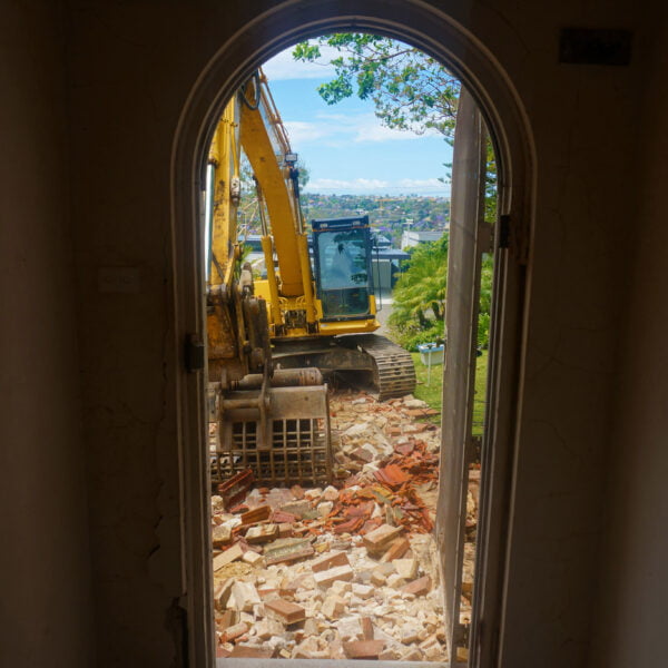 Castle Crag, NSW 2068 15 View through a doorway of a yellow excavator performing home demolitions on a brick structure outside.