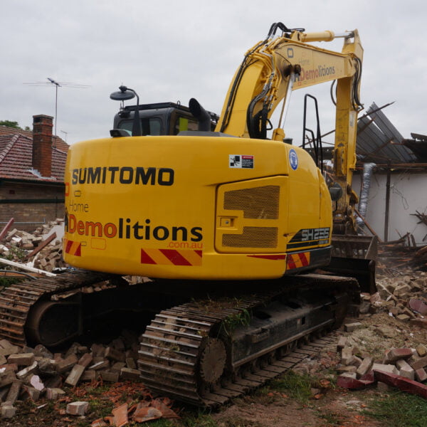 West Ryde, NSW 2114 6 A yellow Sumitomo excavator from a home demolitions company is tearing down a residential building, with debris and rubble scattered around.