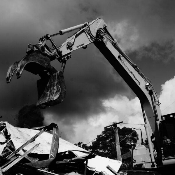 A large excavator with an open claw bucket is in the process of demolishing a pile of debris under a cloudy sky, showcasing the power and efficiency often required in home demolitions.