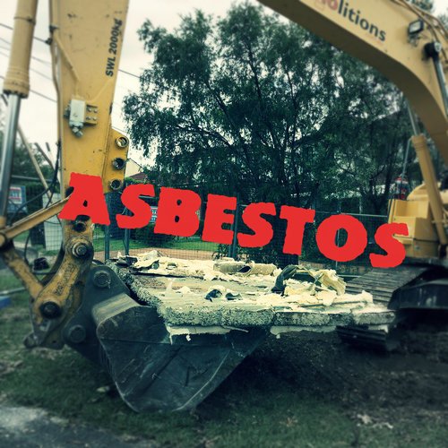 A construction excavator with a bucket containing asbestos debris. The word "ASBESTOS" is prominently displayed in red over the image, highlighting the dangers associated with home demolitions.
