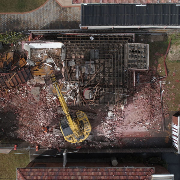 Rod Point, NSW 2046 4 Aerial view of a construction site with a yellow excavator engaged in home demolitions. Debris and rubble are scattered around, and two trucks are parked nearby.