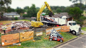 Heavy machinery is demolishing a house, with construction barriers and company signs visible. A truck and a small promotional vehicle for a nearby art gallery are parked nearby, hinting at an upcoming fine art exhibition.