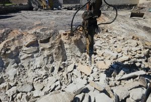 A jackhammer rests on uneven rocky ground during an intensive excavation at the construction site.