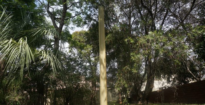 A tall, rectangular monolith stands in the middle of a grassy area surrounded by trees, reminiscent of a site untouched by home demolitions.