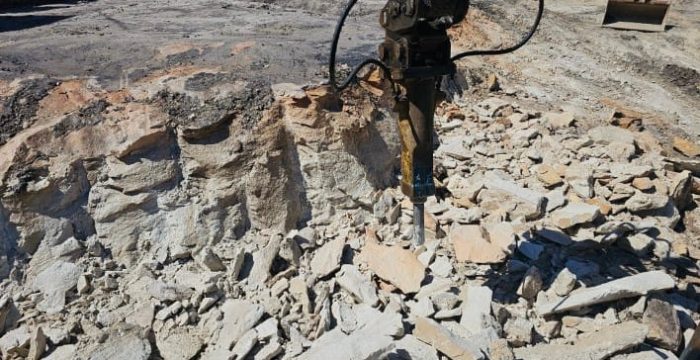 A jackhammer rests on uneven rocky ground during an intensive excavation at the construction site.
